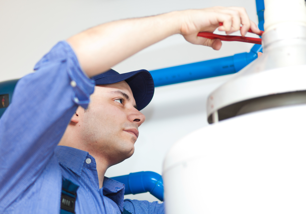man with blue shirt and blue hat holdi g a tool fixing a water heater