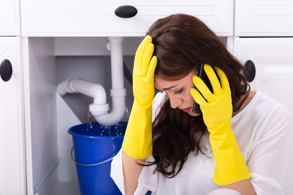 Sad,Young,Woman,Calling,Plumber,In,Front,Of,Water,Leaking